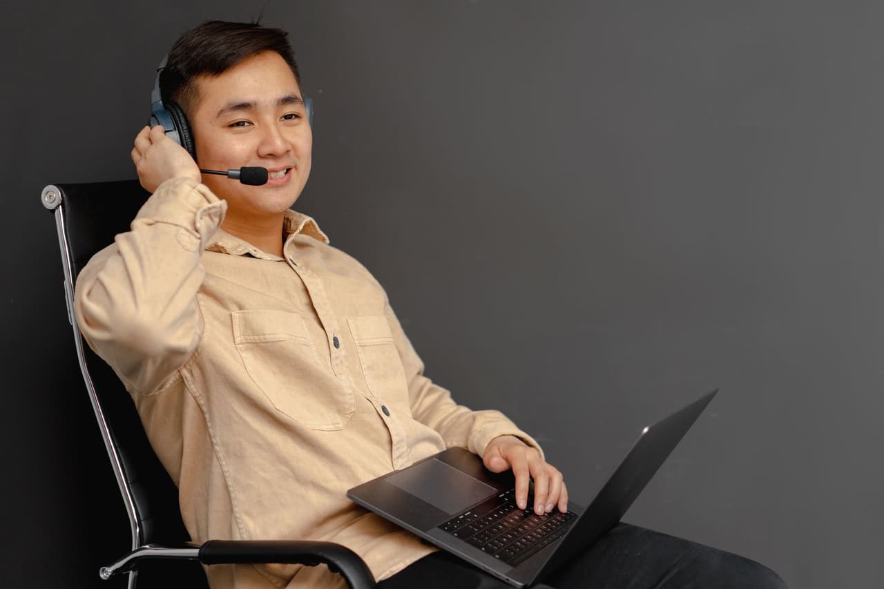 A smiling customer service agent using a laptop and headset
