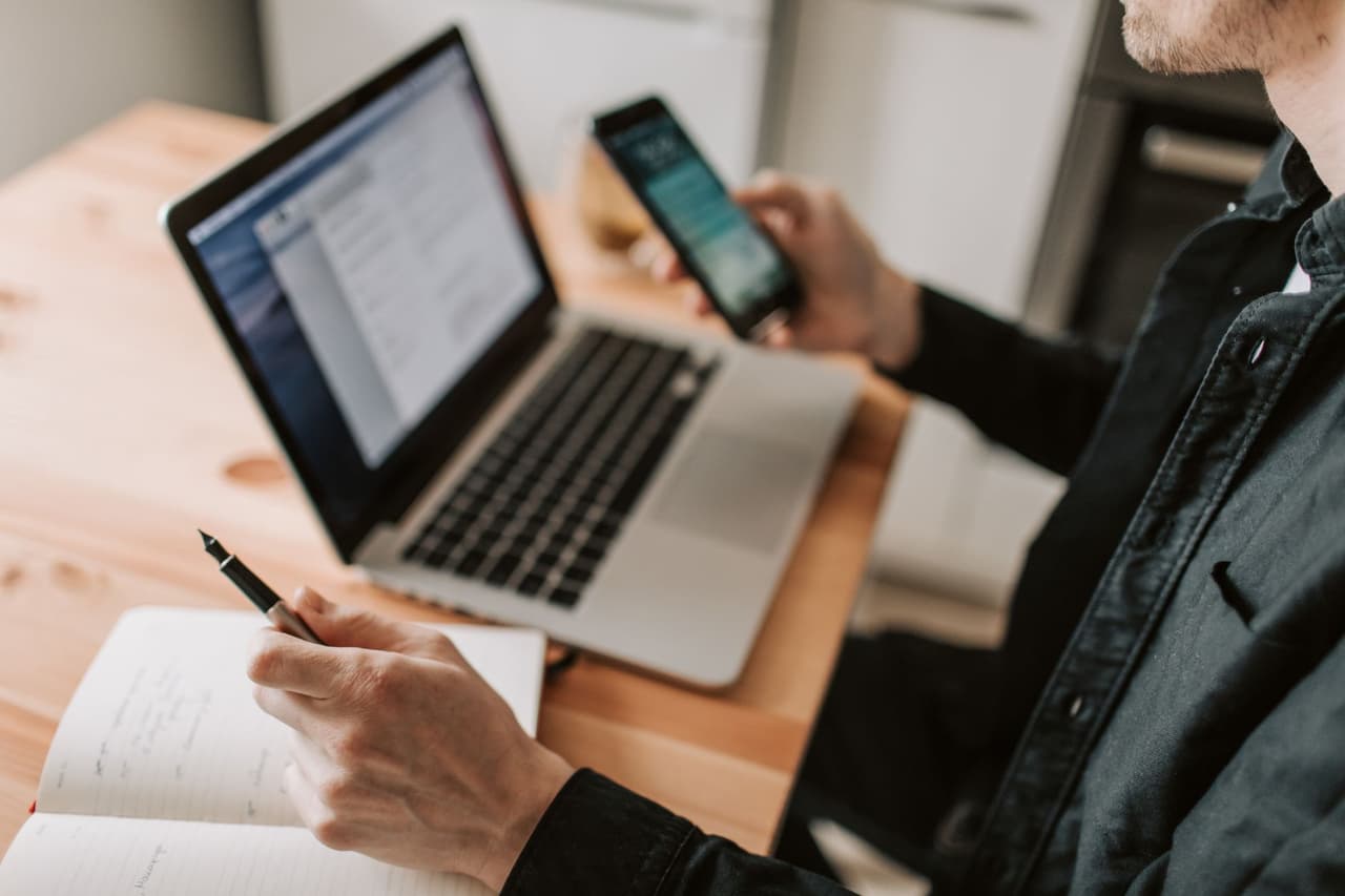 A person setting up WhatsApp Business on a smartphone next to a laptop at a desk