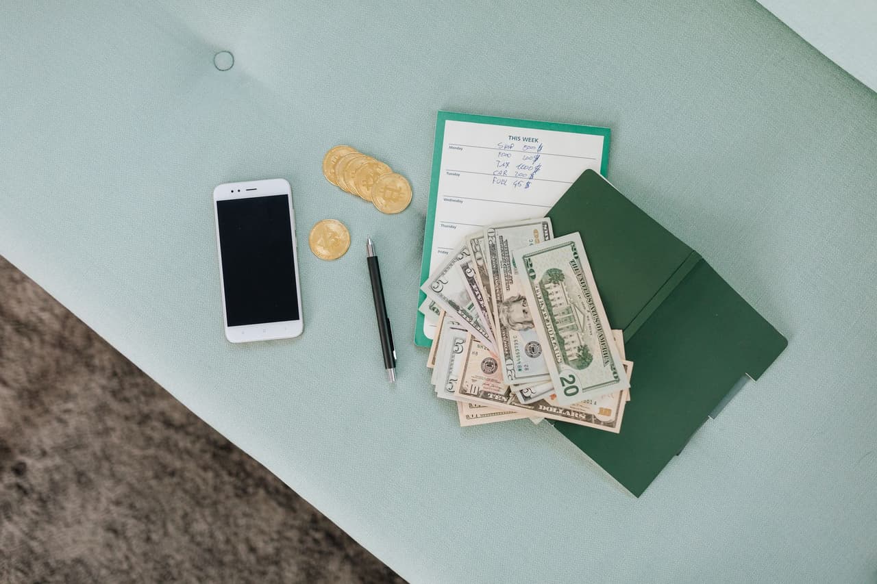 A smartphone with cash, coins, and a planner on a desk