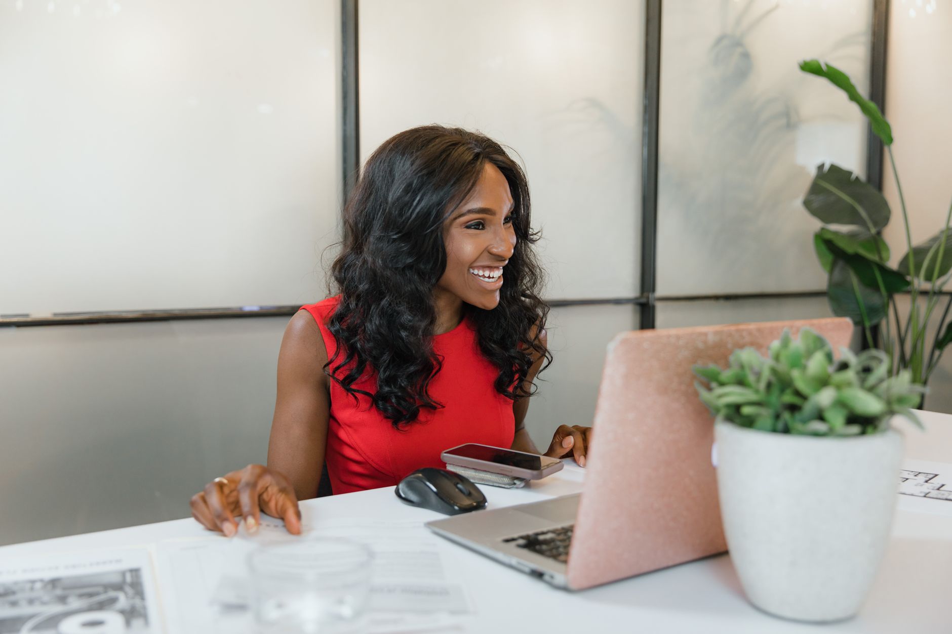 Business owner smiling while using a smartphone and laptop at a desk