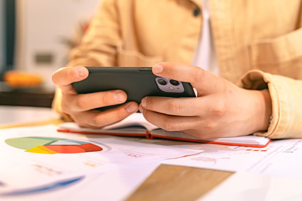 A businessperson checking their phone at a desk with charts