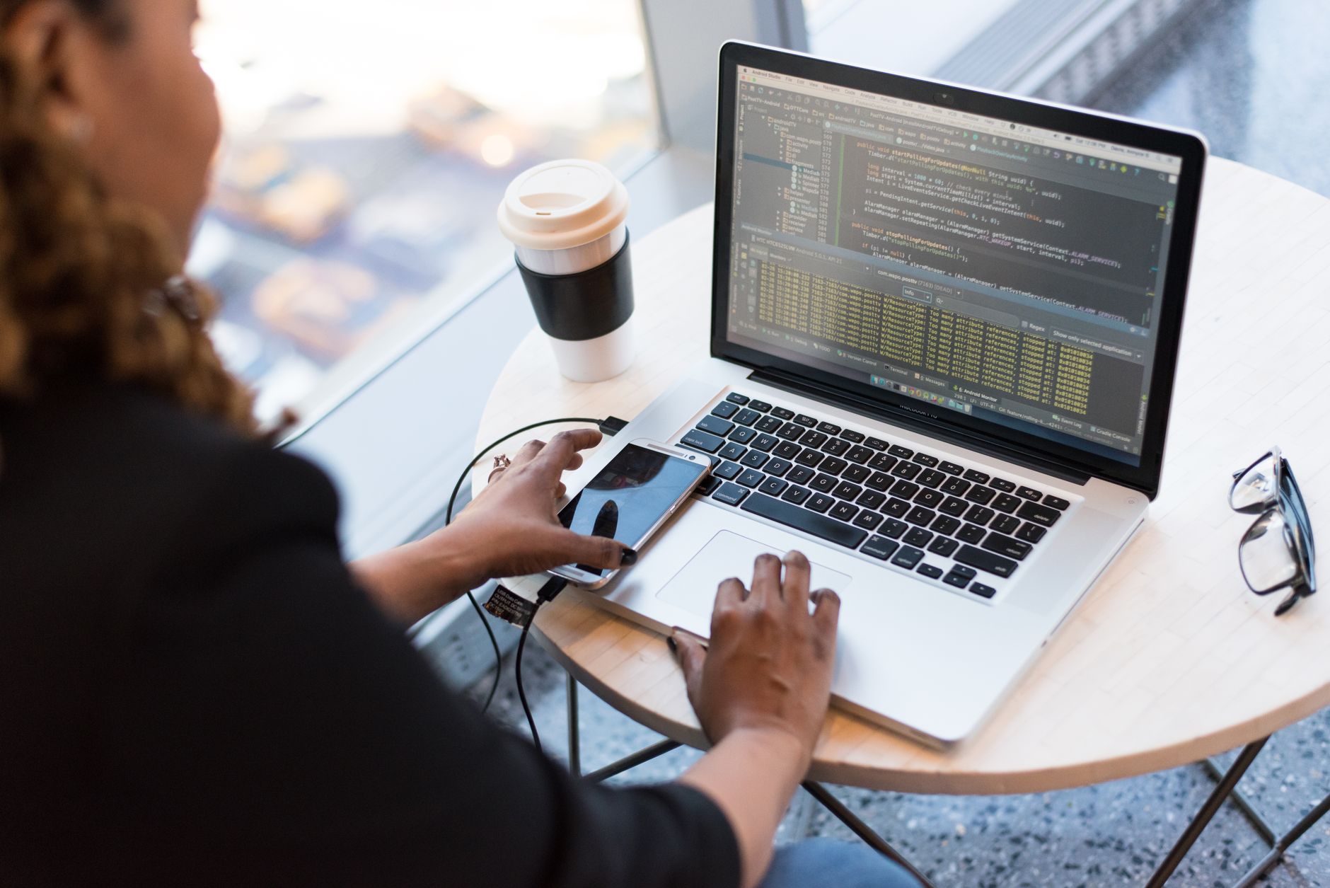 Person setting up software on a laptop with a smartphone and coffee on the desk
