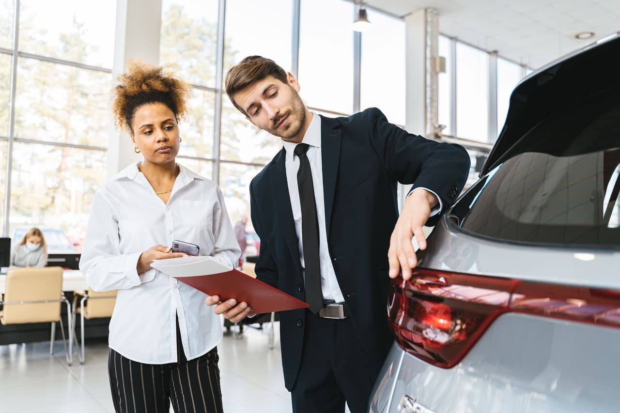 A salesperson showing a car to a customer in a dealership showroom