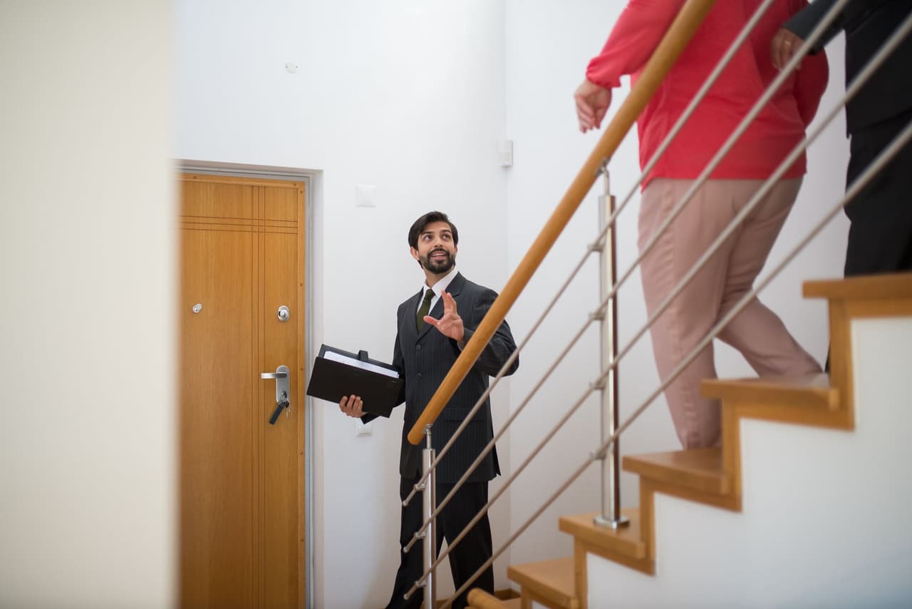 A real estate agent showing a modern home to a couple on the stairs