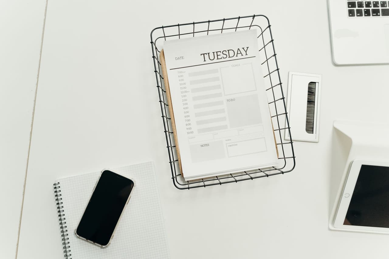 A desk with a smartphone, planner, and gadgets viewed from above